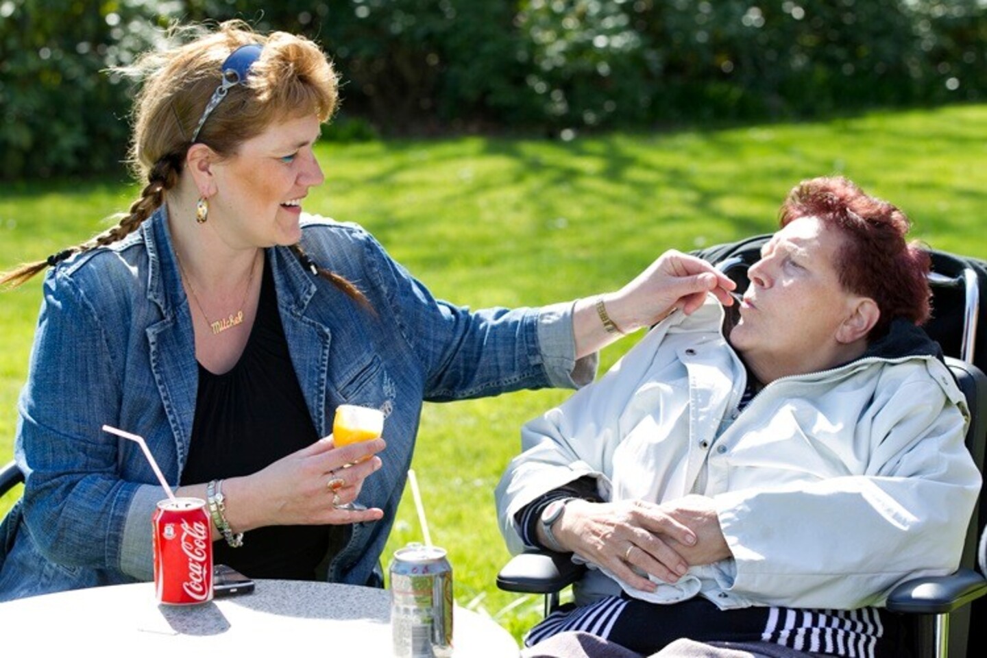 Zorgmedewerker voert een gehandicapte vrouw in rolstoel