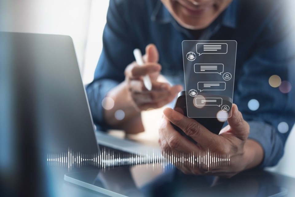 Man voert gesprek met chatbot met gebruik van laptop en smartphone