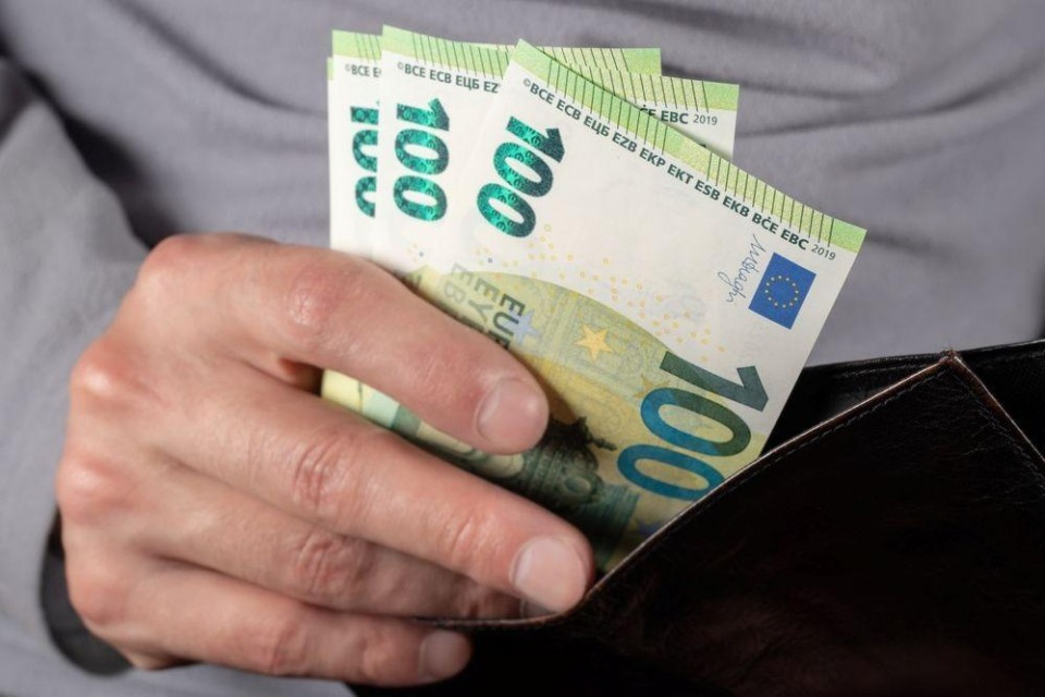 Hand stopt honderdjes in portemonnee