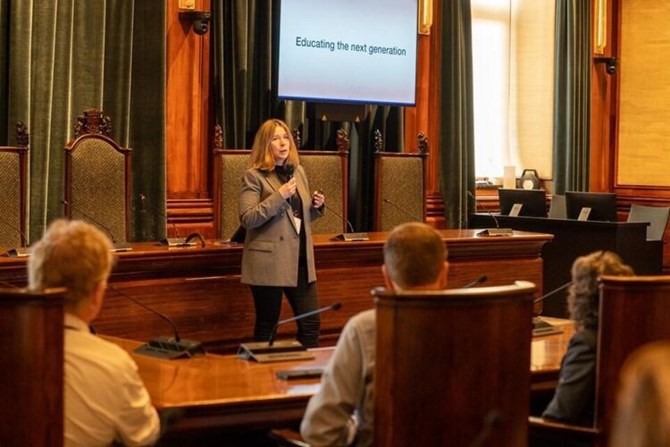 Olga Gadyatskaya spreekt in een houten zaal voor publiek, met het scherm 'Educating the next generation'.