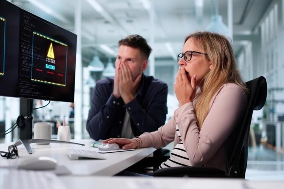 Man en vrouw achter computer die geschrokken kijken naar beeldscherm van Hacked op staat