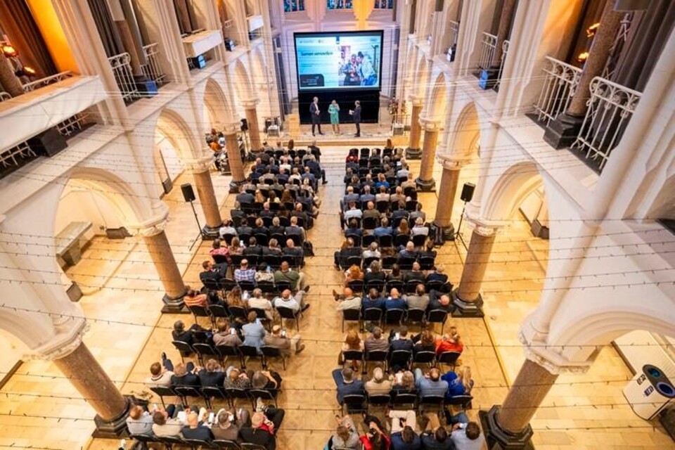 Vogelperspectief conferentiezaal met deelnemers aan tafels en presentatiescherm