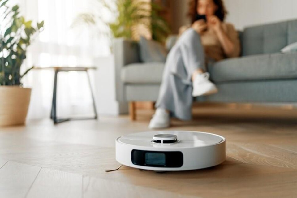 Witte robotstofzuiger op houten vloer in woonkamer met persoon op bank
