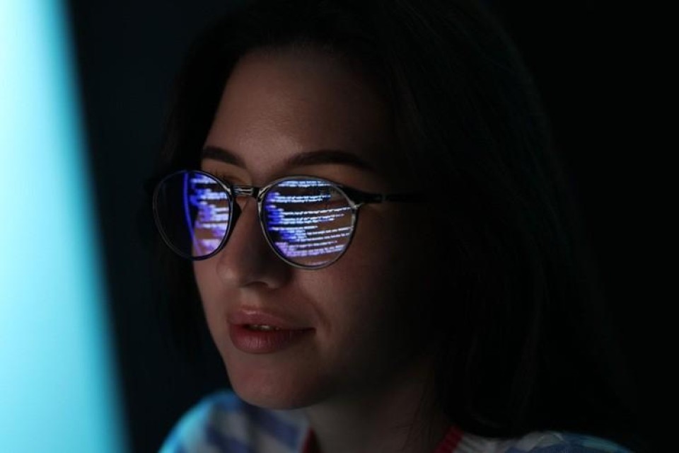 Vrouw met bril op achter computer, in de brilleglazen wordt het beeldscherm weerspiegeld.