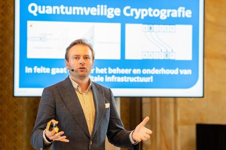 Man in grijs colbert presenteert voor een scherm met de tekst Quantumveilige Cryptografie.