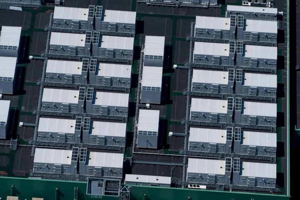 Luchtfoto van datacenters met witte en donkere blokken, groene structuren en technische installaties.