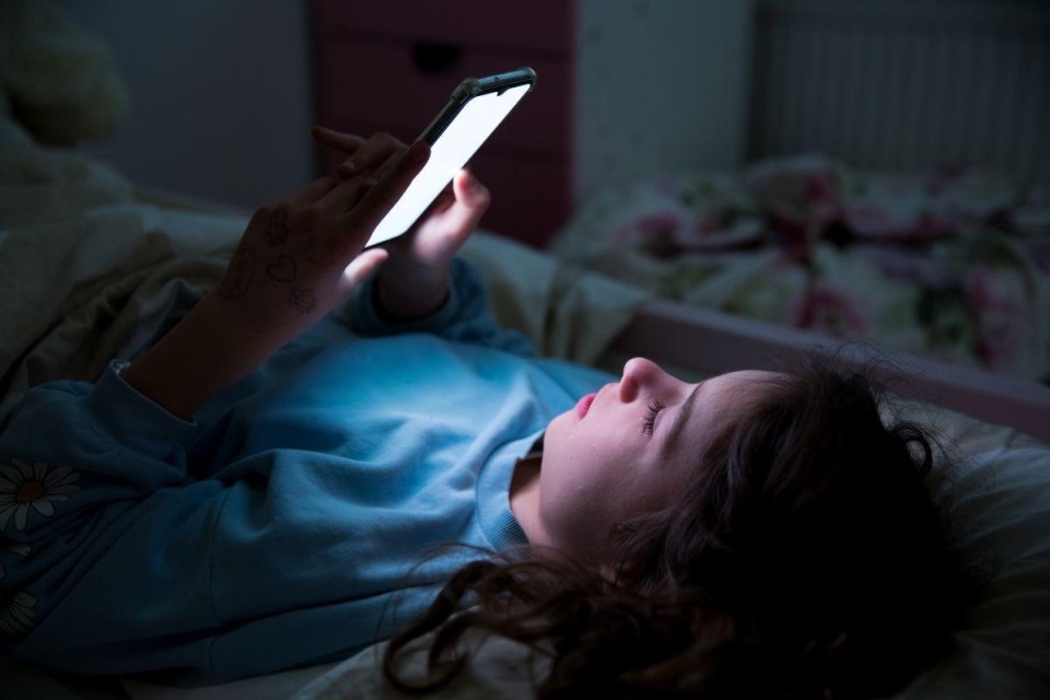 Meisje ligt in bed met mobiele telefoon in haar hand.