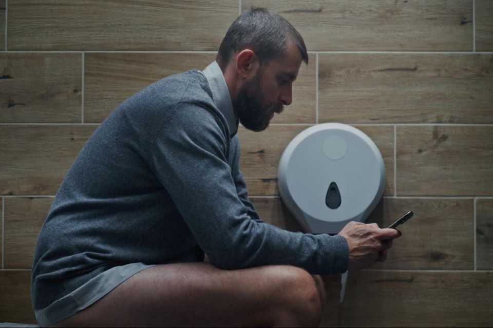 Man met broek op enkels kijkt op zijn smartphone op de wc