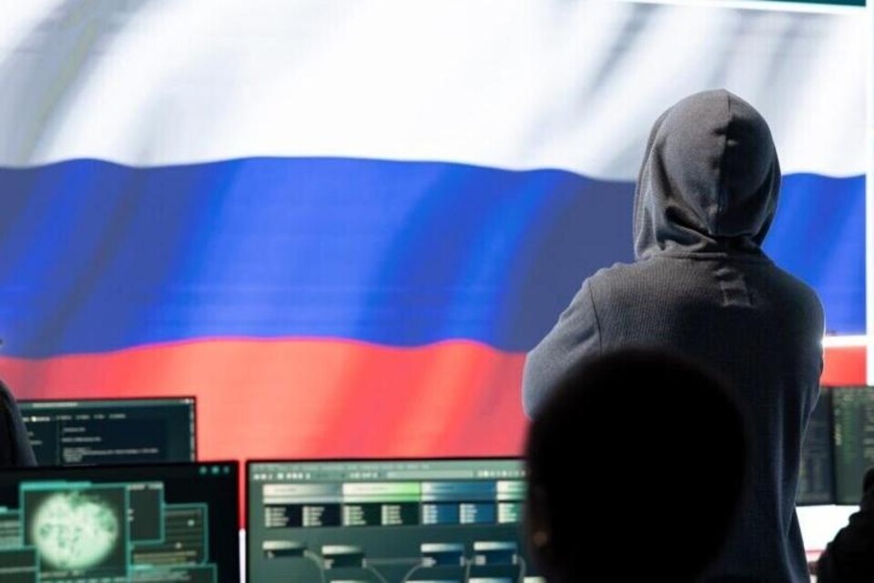 Man in hoodie kijkt naar computerscherm tegen achtergrond Russische vlag