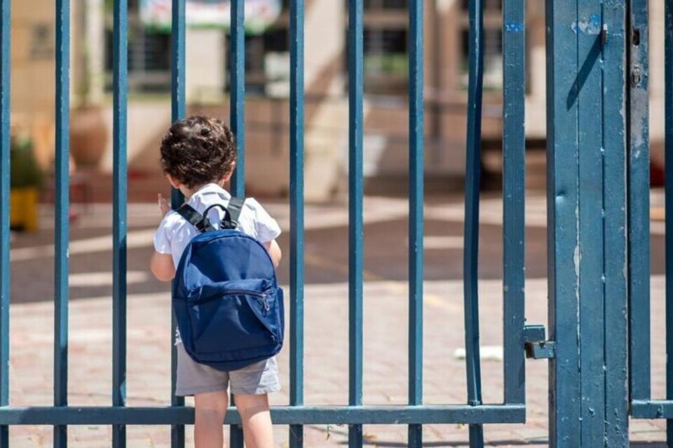 Jongetje met blauwe rugzak voor gesloten schoolhek