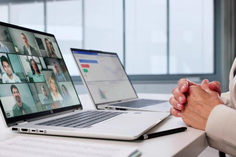 vrouw zit te videovergaderen met 2 laptops voor zich