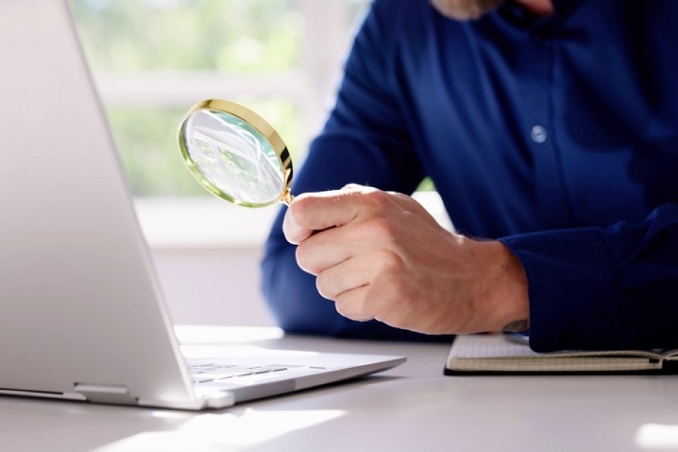 man kijkt met loep naar informatie op laptop